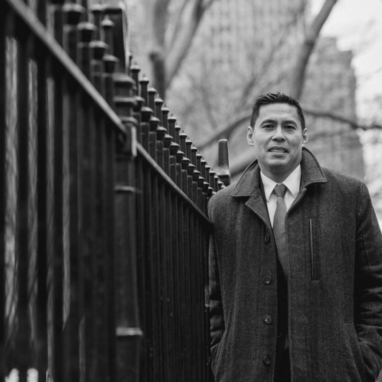 man in suit posing next to a fence