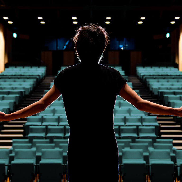 woman standing on stage facing theatre