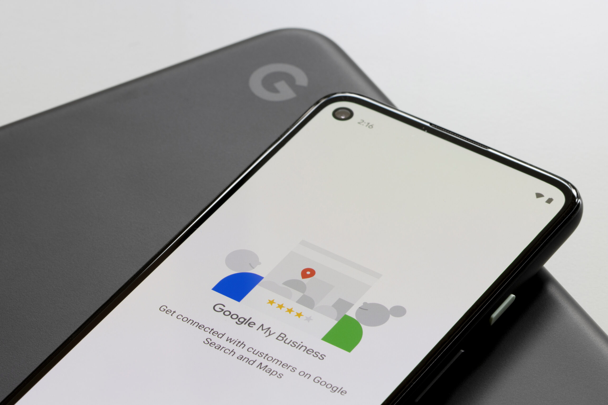 A smartphone displays the Google My Business app welcome screen, resting on a closed, dark gray laptop with a visible Google logo.