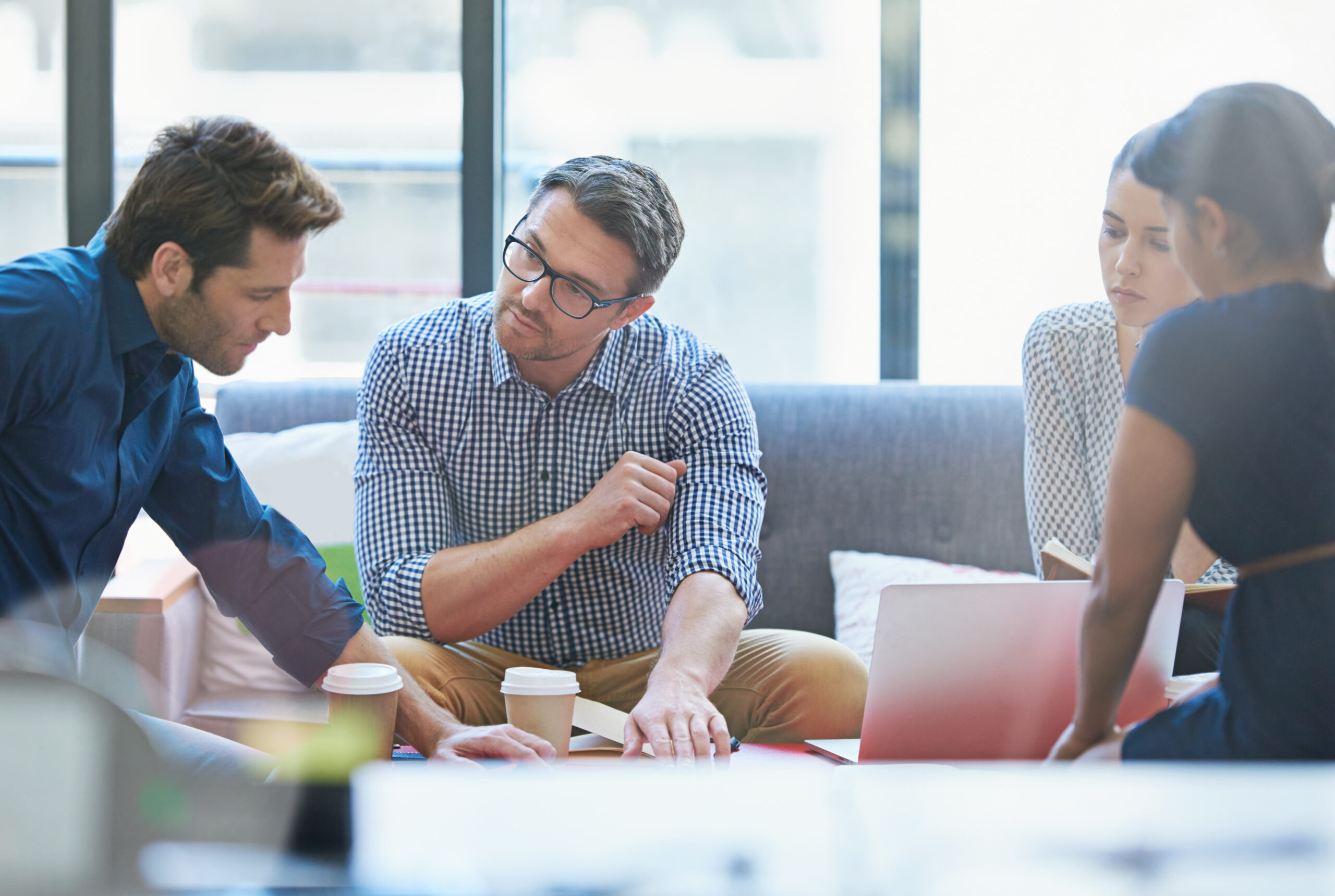 Four people sit together in an office setting, discussing documents and laptops over coffee as they review important Questions To Ask Your Web Agency.