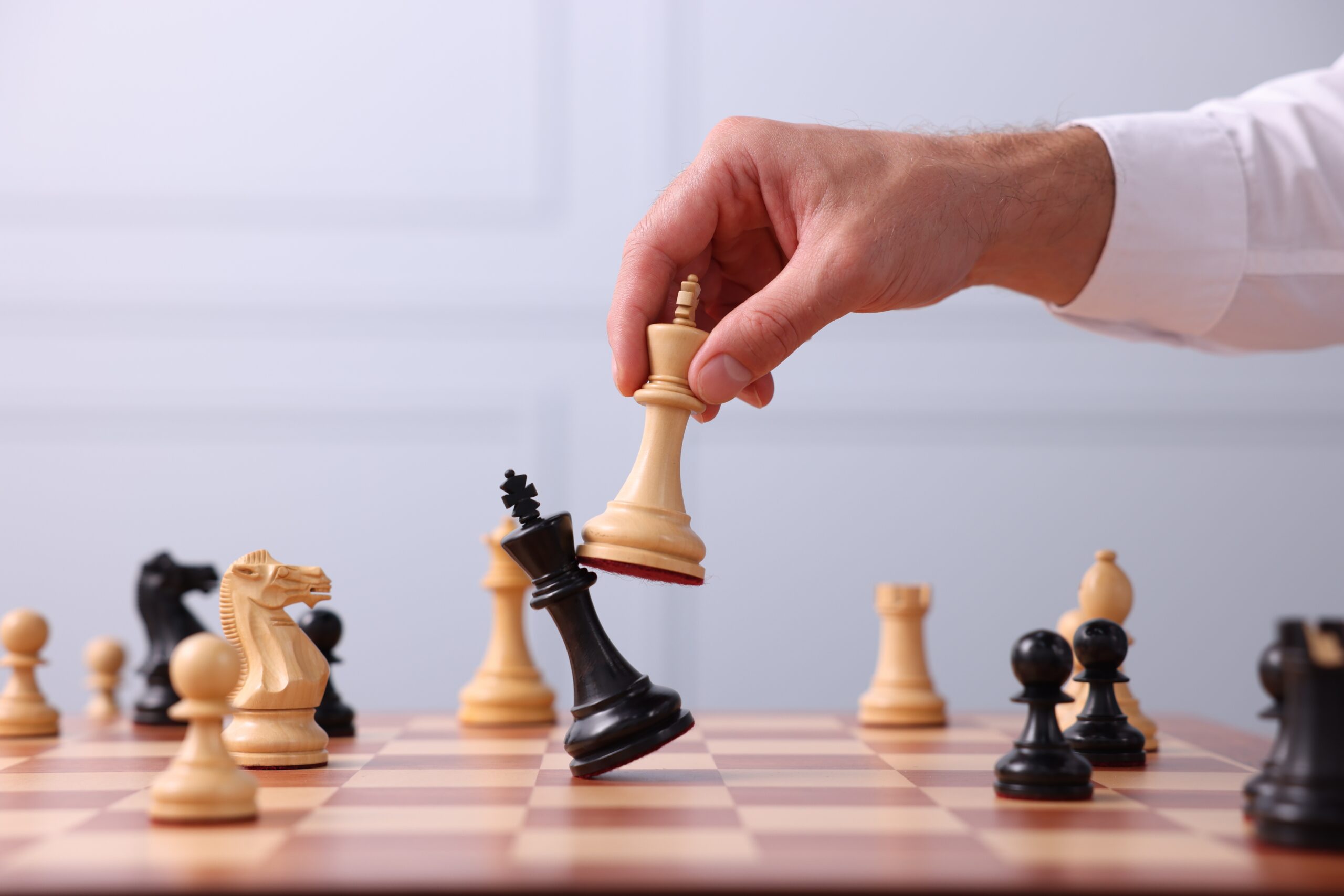 A hand moves a white king to capture a black king on a chessboard, with various chess pieces visible in play.