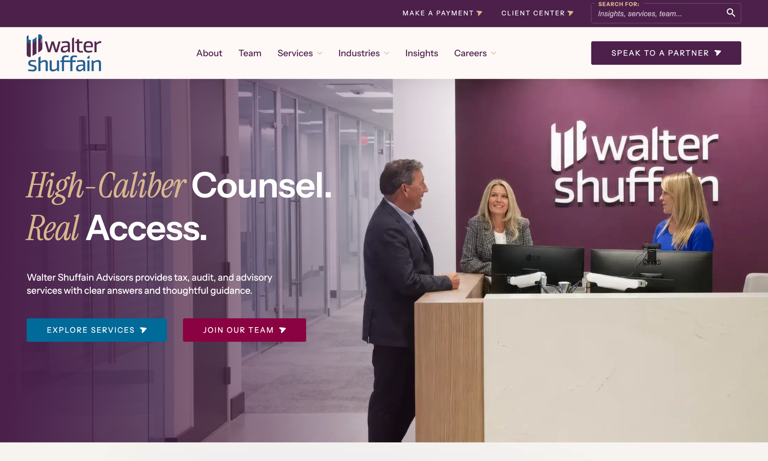 Three people talk at the reception area of the Walter Shuffain office, with company branding visible on the wall and a desk with computers in front of them.